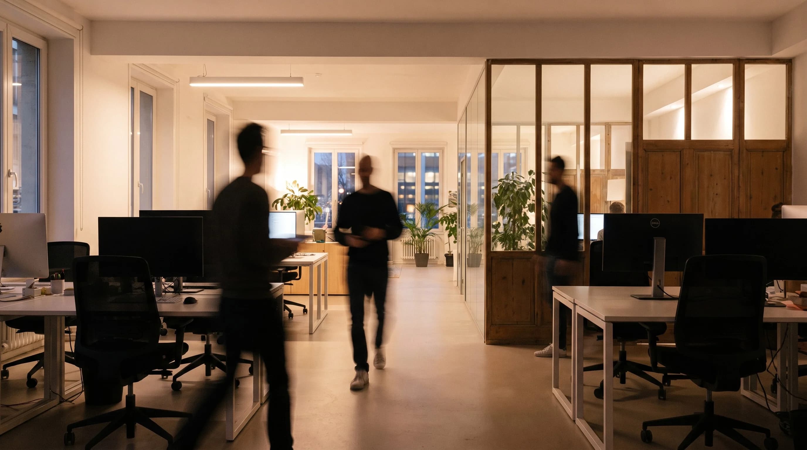 Ambiance de bureau dirigée en IA : circulation d'un open space vitré, cloisons verrières et bois clair, silhouettes de collaborateurs en mouvement