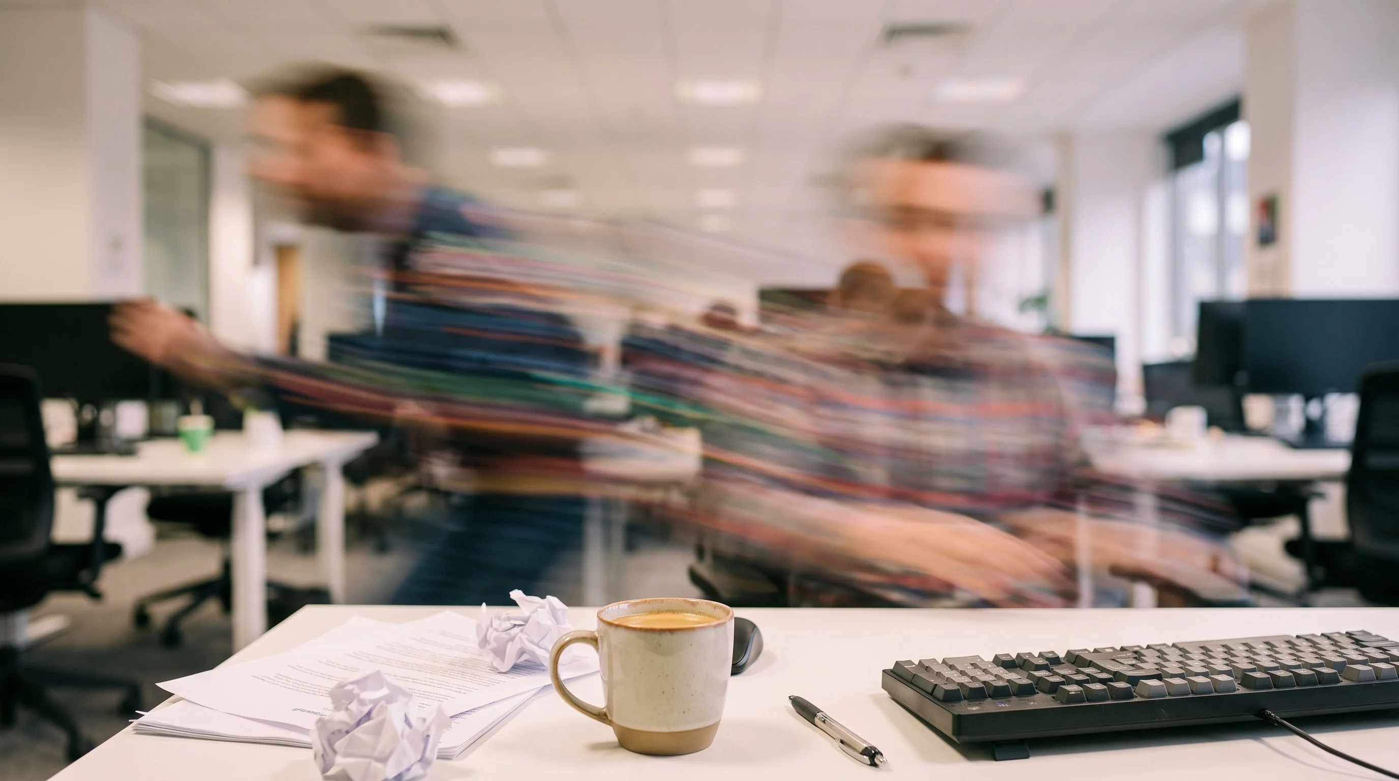 Ambiance de bureau dirigée en IA : open space en enfilade, collaborateurs saisis en mouvement, tasse et clavier au premier plan