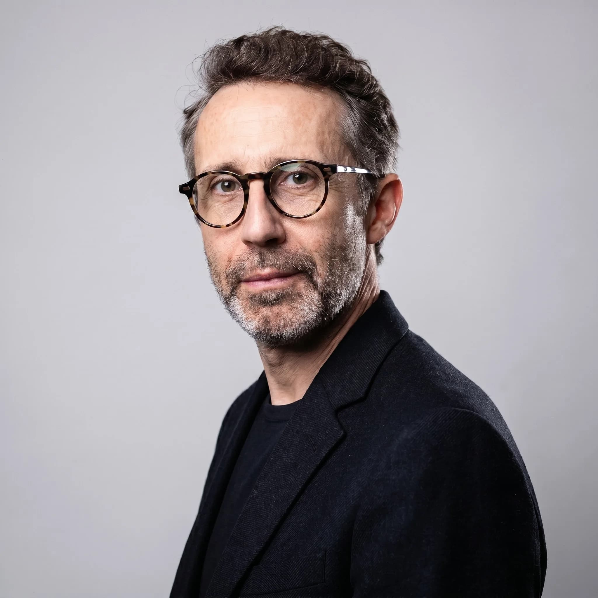 Directed corporate portrait delivered by the studio: man in a black jacket on a plain light grey background, steady gaze to camera.