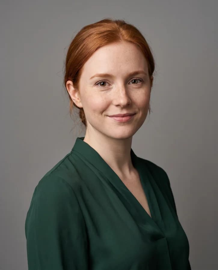 Portrait corporate d’une jeune femme rousse, chemisier vert sapin, fond gris studio (démonstration, personne fictive)