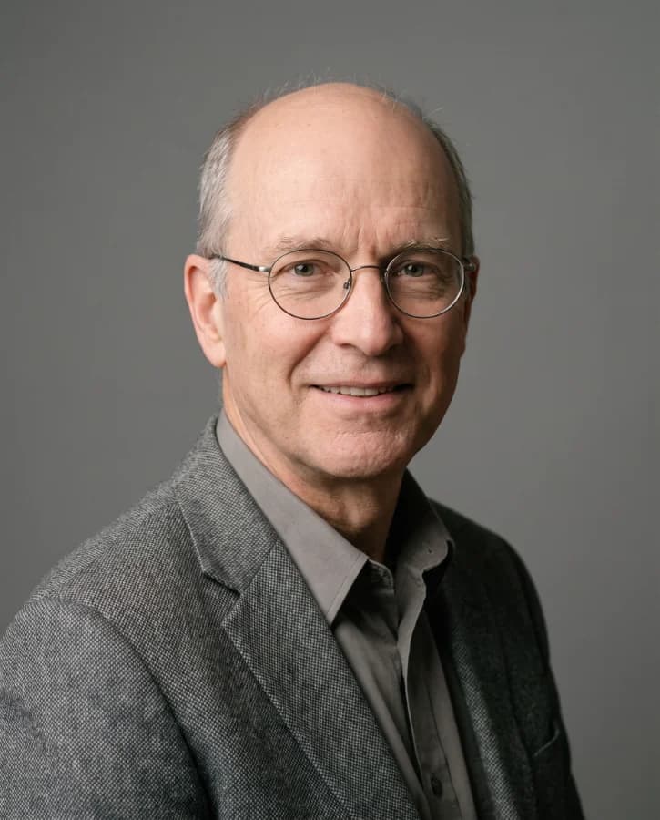 Portrait corporate d’un homme d’une soixantaine d’années, lunettes rondes, veste de tweed gris, fond gris studio (démonstration, personne fictive)