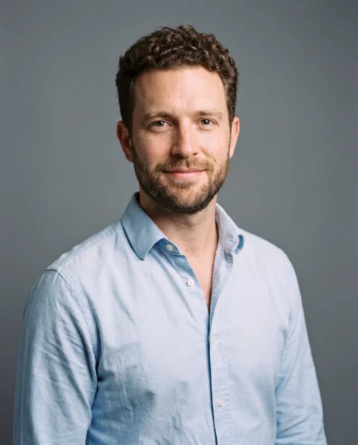Portrait corporate d’un homme d’une trentaine d’années, cheveux bouclés, chemise oxford bleu clair, fond gris studio (démonstration, personne fictive)