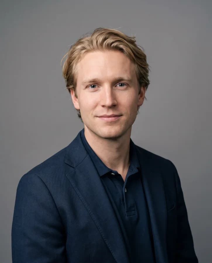 Portrait corporate d’un jeune homme blond, polo marine sous veste, fond gris studio (démonstration, personne fictive)